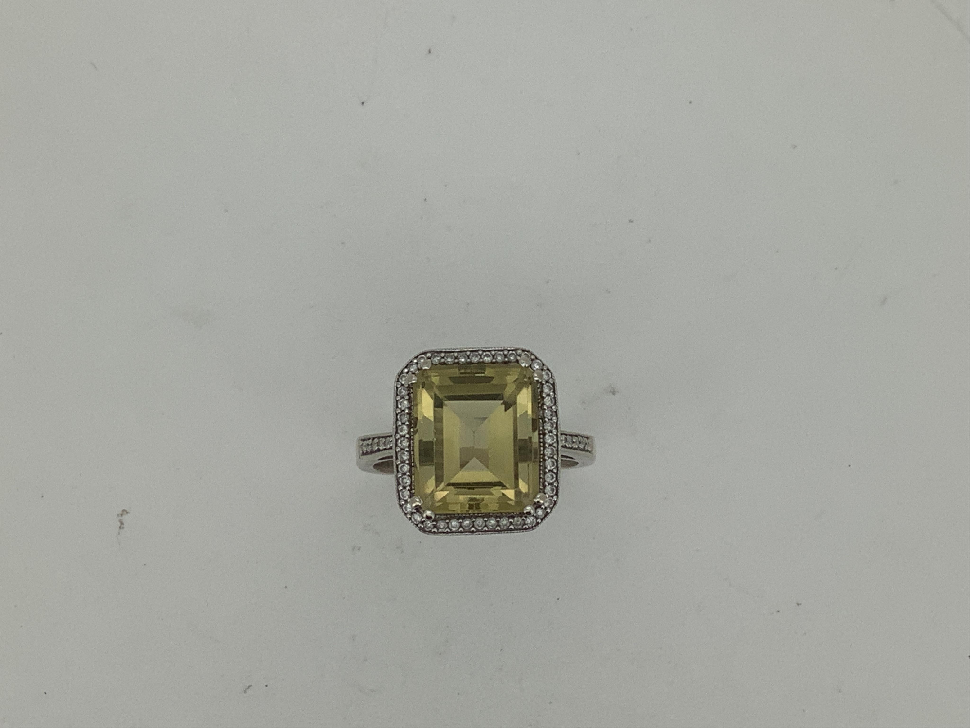 A modern 18k white metal and single stone emerald cut citrine ring, with diamond chip set border and shoulders, size R/S, gross weight 5.9 grams, the citrine measuring approximately 11.9mm, by 10.1mm.